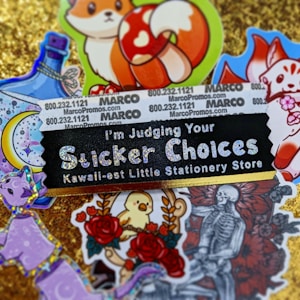 A collection of colorful and whimsical stickers displayed on a glittery gold background. The central black sticker with glittery text reads 'I'm Judging Your Sticker Choices' followed by 'Kawaii-est Little Stationery Store.' Surrounding this sticker are various images, including a fox with a red and white mushroom, a bottle with ribbons, a crescent moon with stars, a purple cat, a bird amidst roses, and a monochrome skeletal figure with a bouquet of roses. Some promotional text and numbers appear on a white background towards the top.
