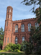 A stately traditional school building in dark purple and white, surrounded by lush greenery under a clear sky.