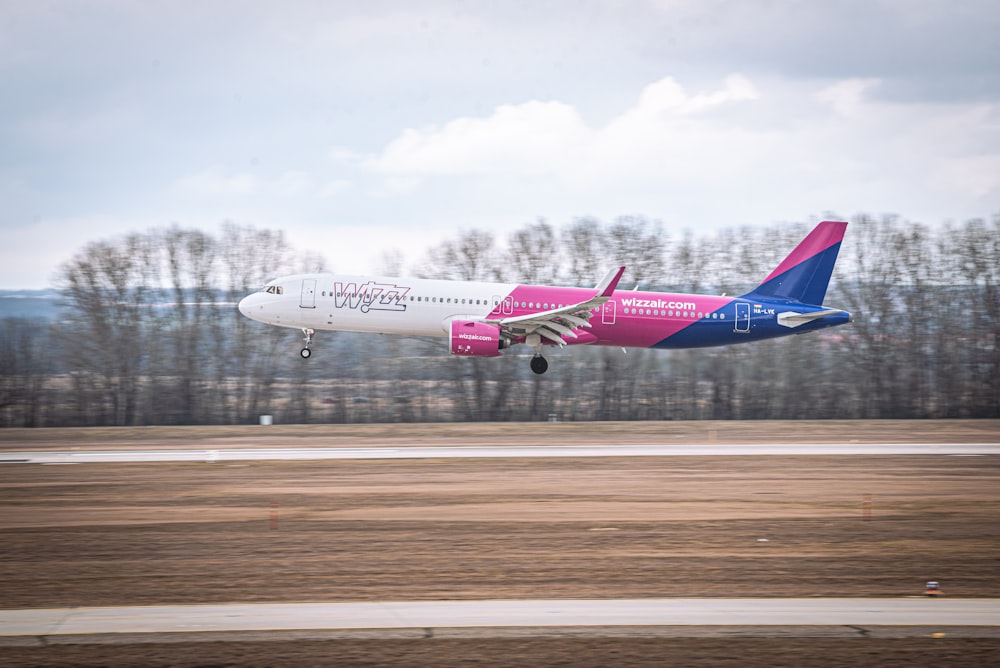 a pink and blue plane taking off from a runway