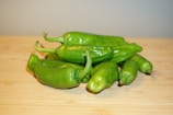 A bunch of fresh green chilies arranged on a wooden surface.