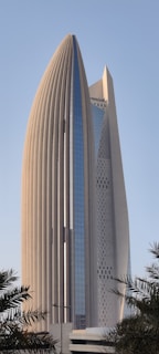 A modern skyscraper with an innovative design characterized by curved, vertical architectural elements and a sleek, glass facade. The structure is surrounded by palm trees, adding a touch of greenery to the urban environment.