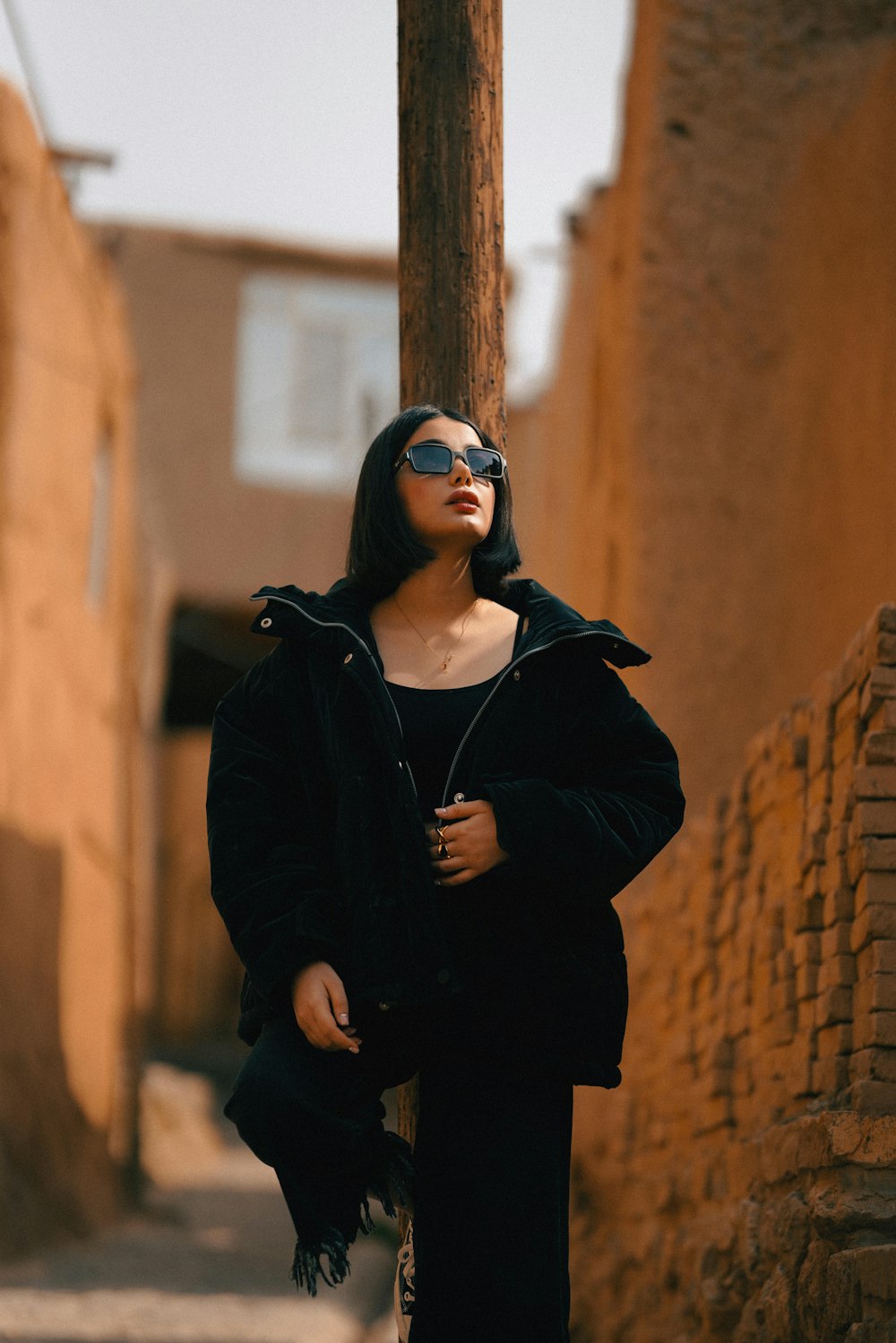 a woman leaning on a pole in an alley