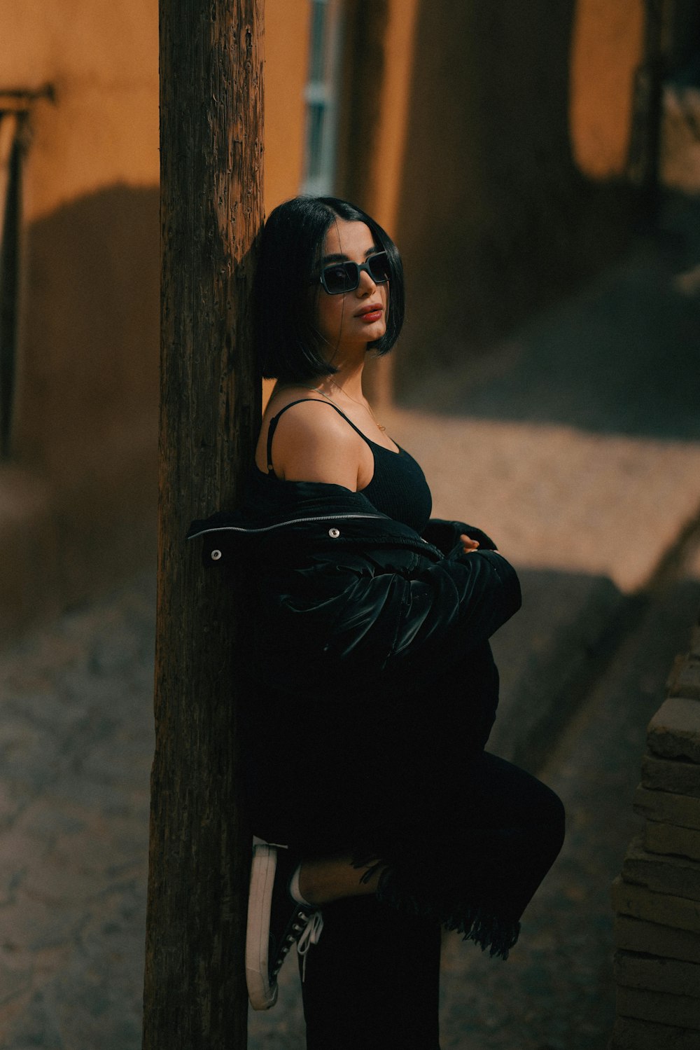 a woman leaning against a pole on a street