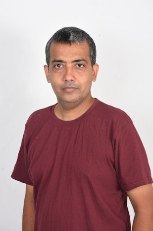 A person with short, dark hair is wearing a maroon t-shirt. They are standing against a plain white background, looking directly at the camera with a neutral expression.