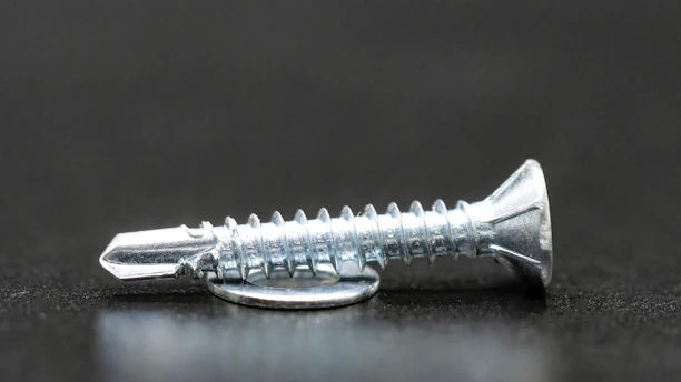 Close-up photo of a stainless steel screw being inspected under bright factory lighting.