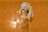 A Lego figurine is crouching and gazing intently at a shiny gold ring placed on a textured, orange surface. The figure has piercing blue eyes and an expression of fascination, resembling a well-known character from literature.