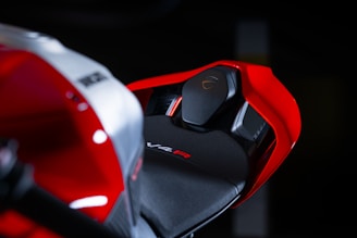 A close-up view of a motorcycle seat and rear section. The design is sleek and modern, featuring angular shapes with a red and black color scheme. The V4 R branding is visible on the seat, indicating a high-performance model.