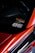 A close-up view of the corner of a car with a sleek, red finish and carbon fiber detailing. A decal is visible on the window with the text 'Ignition Auto Repairing' in orange and '86' in white. The car's glossy surface reflects light, adding to its dynamic and sporty aesthetic.