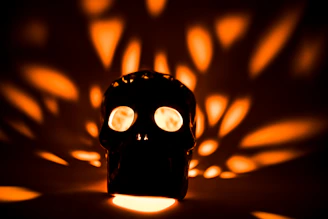 An artistic skull-shaped candle holder casting warm shadows on a wooden shelf.