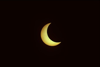 A crescent-shaped celestial body appears against a dark background, hinting at a solar eclipse.