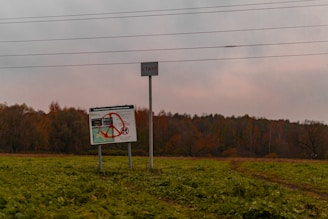 a sign in the middle of a field with trees in the background