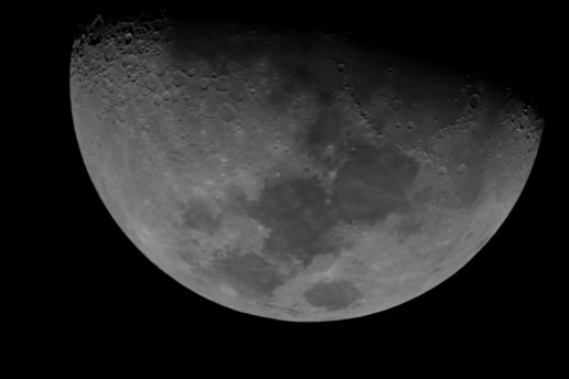 A detailed view of the moon's surface, showcasing craters and lunar maria against a dark space background. The illuminated portion reveals textures and shadows.