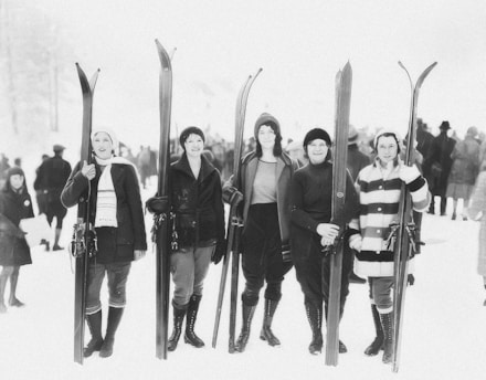 A group of female ski patrollers gathered on a snowy mountain slope, smiling and preparing for an event.