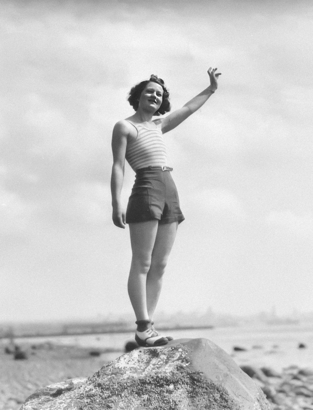 a woman standing on top of a rock on a beach