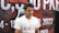 A person wearing a white t-shirt with the word 'TRAVE' partially visible is seated in front of a backdrop with text in large, bold letters and numbers. The backdrop includes information such as a prize pool mention and a date in 2023, featuring a predominantly red and black color scheme.