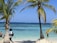 Smiling travelers enjoying a sunset on a tropical beach with clear blue waters.