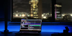 A student focused intently on coding a project late at night with neon blue light illuminating their workspace