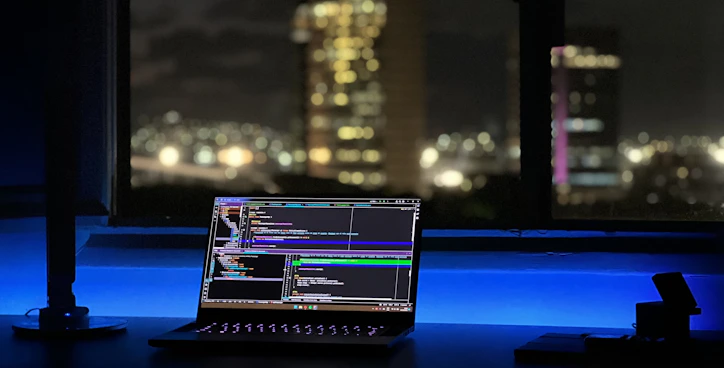A focused web designer working on a sleek laptop with a vibrant US city skyline in the background.