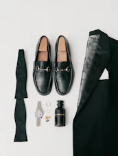 A modern flat lay of traditional men's wear accessories including a peacock feather brooch, gold cufflinks, and a cream shawl.