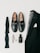 A collection of men's formal accessories neatly arranged includes black loafers with silver accents, a folded black bow tie, a black suit jacket with a patterned lining, a black bottle of cologne, a silver wristwatch, a pair of rings, and gold cufflinks.