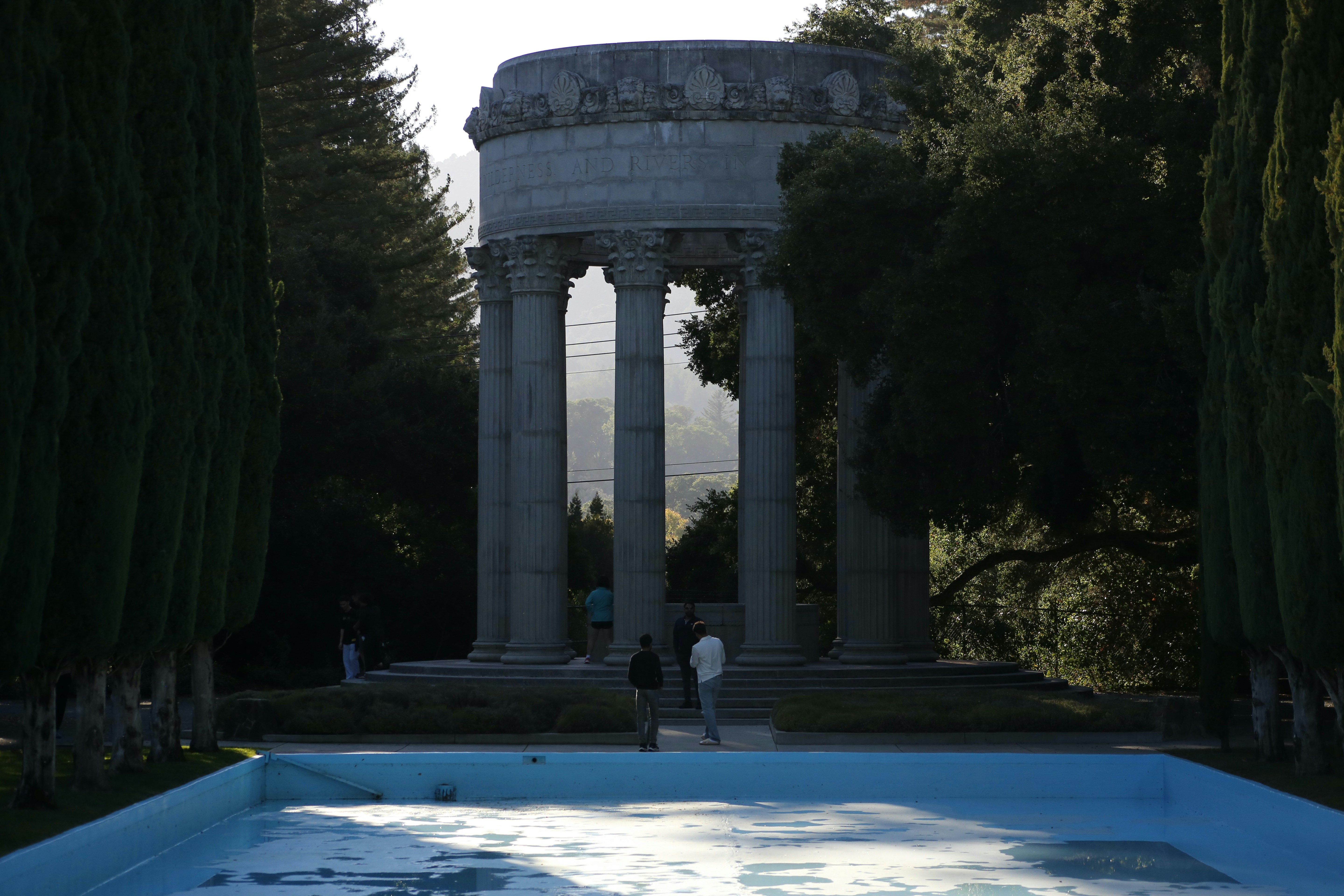 two people standing in front of a pool surrounded by trees