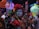 A group of people is dressed in traditional, colorful attire with intricate face paint resembling sugar skulls. They are holding vibrant paper lanterns and decorative crafts, appearing to celebrate a cultural event at night.