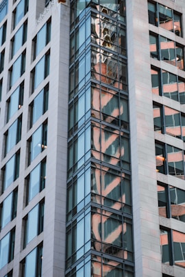 a tall building with a reflection of a clock on it's side