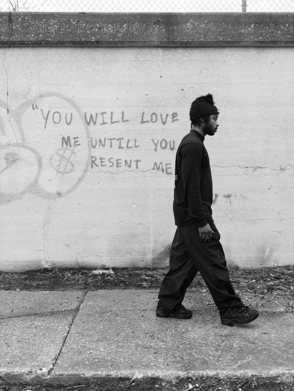 a man walking down a sidewalk next to a wall