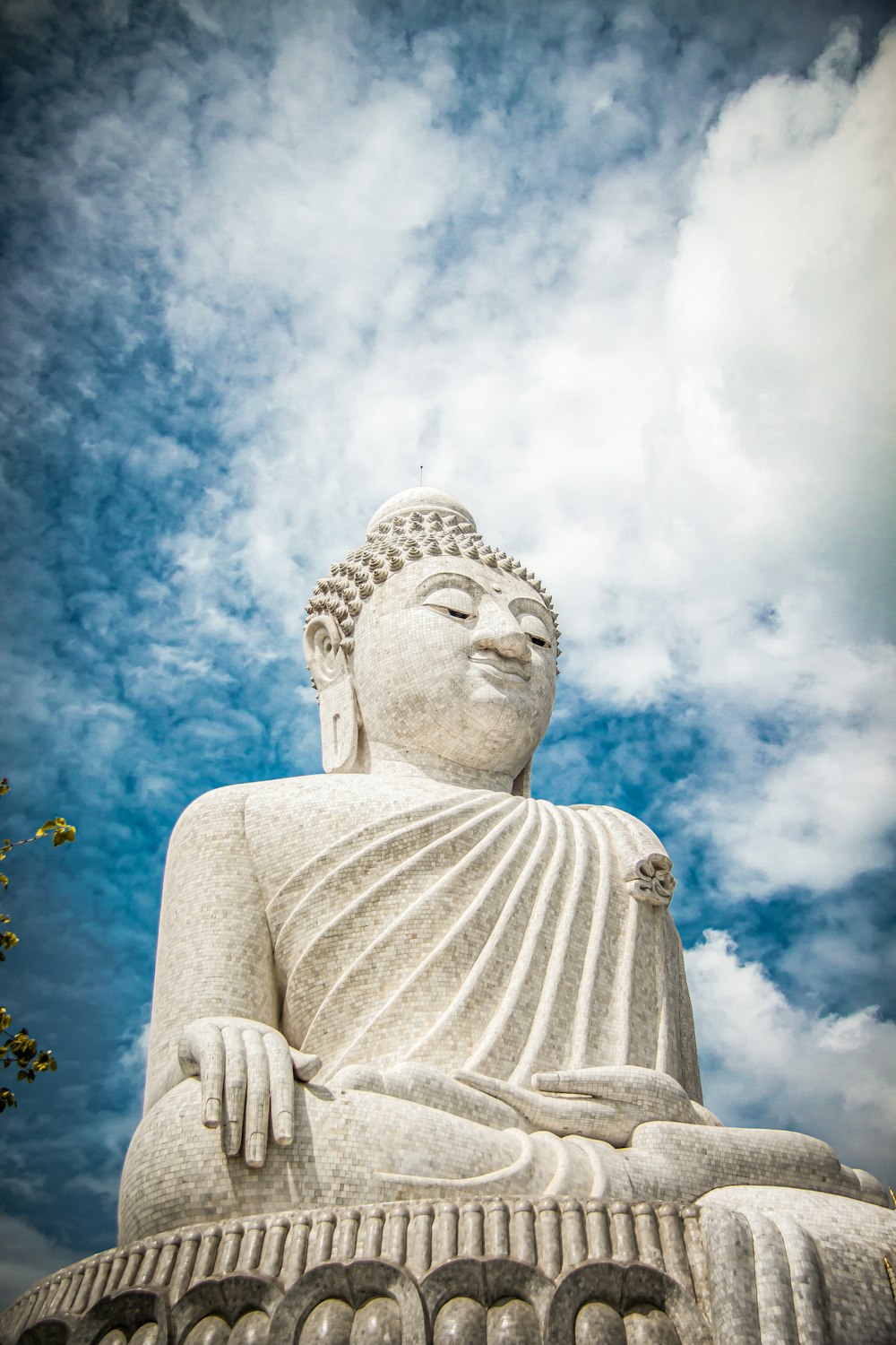 a buddha statue sitting under a cloudy blue sky