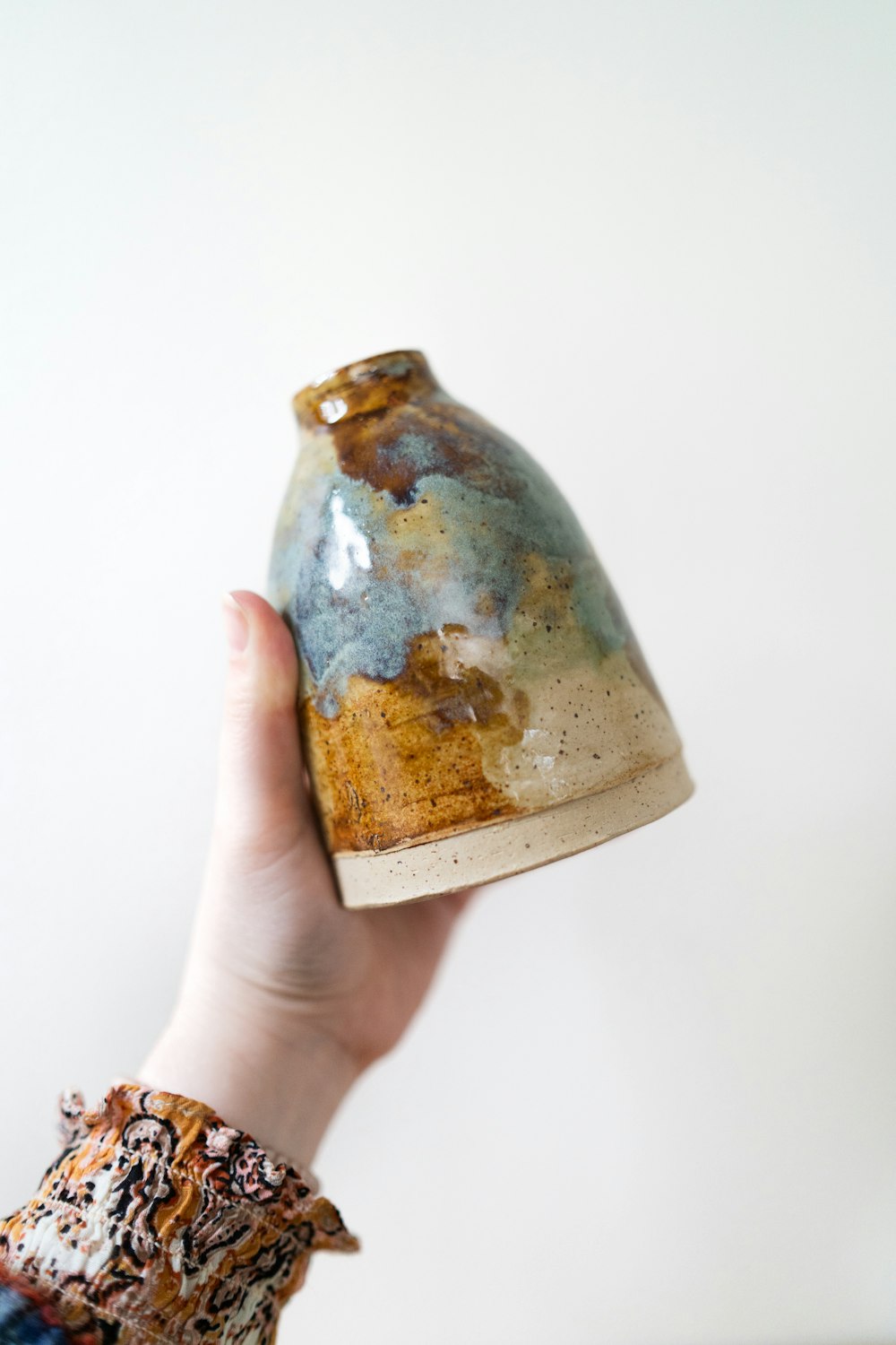 a hand holding a ceramic vase in the air