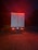 A large truck is parked on a gravel surface, illuminated by red taillights in a dimly lit environment. The vehicle has flags of Canada and the United States on its rear doors, with additional reflective markings and safety signs visible. The surrounding area is dark, hinting at nighttime or early evening.
