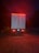 A large truck is parked on a gravel surface, illuminated by red taillights in a dimly lit environment. The vehicle has flags of Canada and the United States on its rear doors, with additional reflective markings and safety signs visible. The surrounding area is dark, hinting at nighttime or early evening.