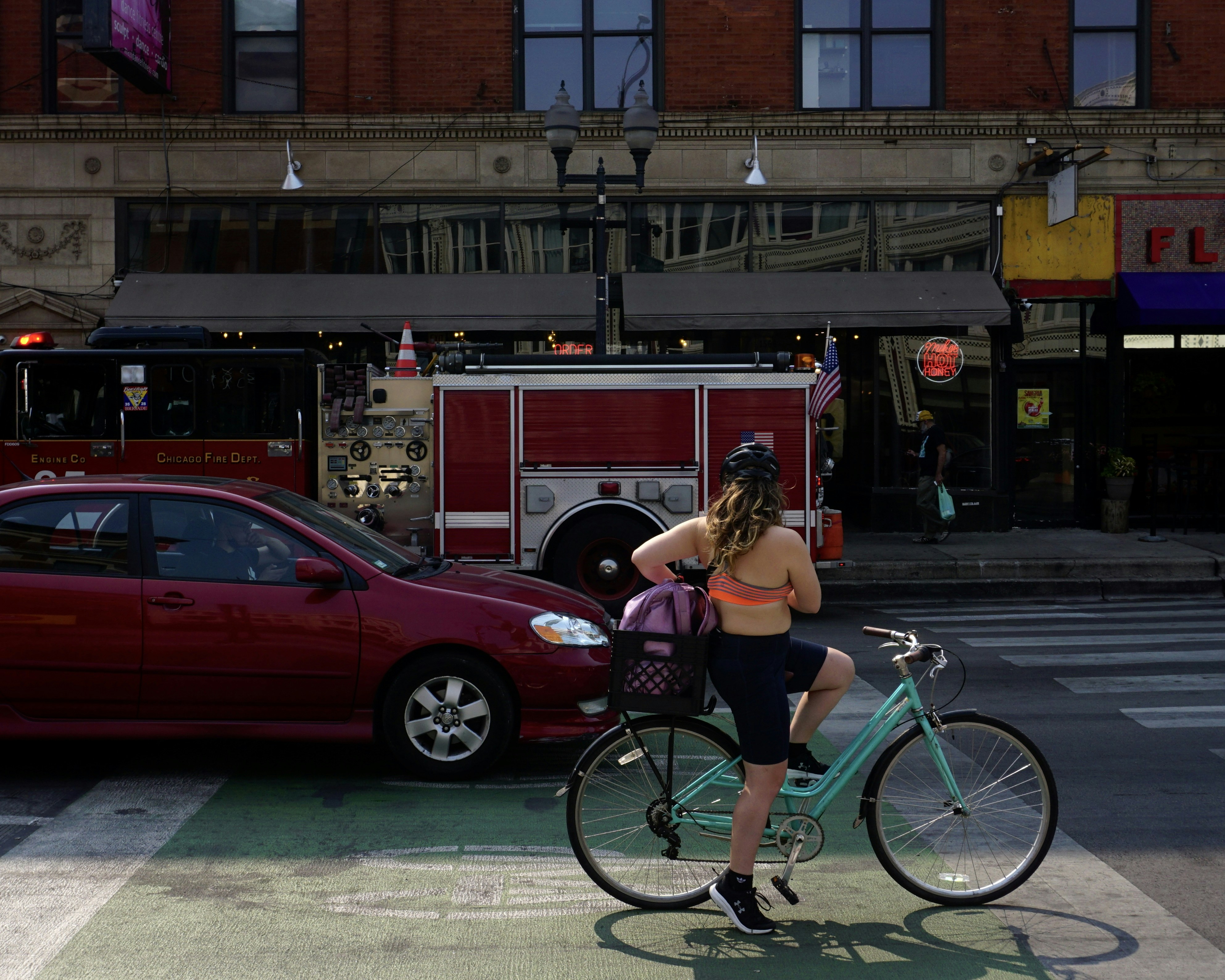 a woman riding a bike down a street next to a fire truck, Situated at Wicker Park, Chicago, Illinois, view of a lady riding a bicycle for evening exercise surrounded by vehicles passing by.