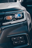 Close-up view of a car's headlight featuring advanced LED technology. The headlight is prominently displayed, showcasing intricate details and modern design elements, including a blue-tinted reflective surface and sleek contours.