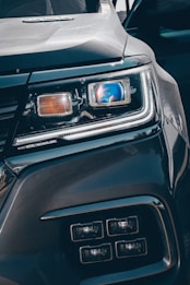 Close-up view of a car's headlight featuring advanced LED technology. The headlight is prominently displayed, showcasing intricate details and modern design elements, including a blue-tinted reflective surface and sleek contours.