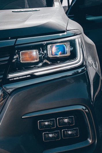 Close-up view of a car's headlight featuring advanced LED technology. The headlight is prominently displayed, showcasing intricate details and modern design elements, including a blue-tinted reflective surface and sleek contours.