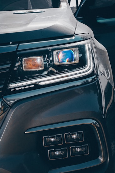 Close-up view of a car's headlight featuring advanced LED technology. The headlight is prominently displayed, showcasing intricate details and modern design elements, including a blue-tinted reflective surface and sleek contours.