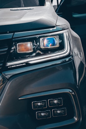 Close-up view of a car's headlight featuring advanced LED technology. The headlight is prominently displayed, showcasing intricate details and modern design elements, including a blue-tinted reflective surface and sleek contours.