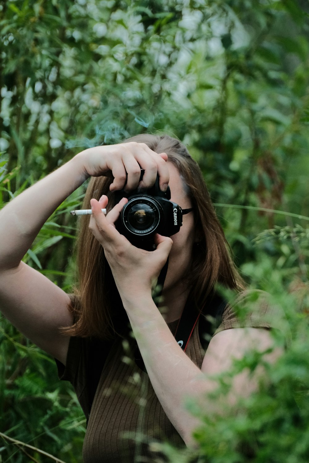 a woman taking a picture with a camera in a forest