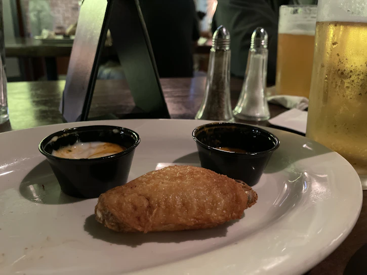 Close-up of a spicy red wing sauce dripping off a crispy chicken wing.