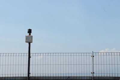 Technician installing a green military-colored perimeter fence with digital security cameras in a small business setting.