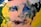 An abstract painting with swirling patterns and vibrant colors, featuring a human-like face with expressive brush strokes. The face is crafted by overlaying shades of pink with dark blue, green, and yellow accents, creating a sense of movement and depth.