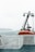 A lifeboat is secured on the deck of a ship. The deck is surrounded by white metal railings, and the background shows a misty sea with an overcast sky. An island can be seen in the distance.