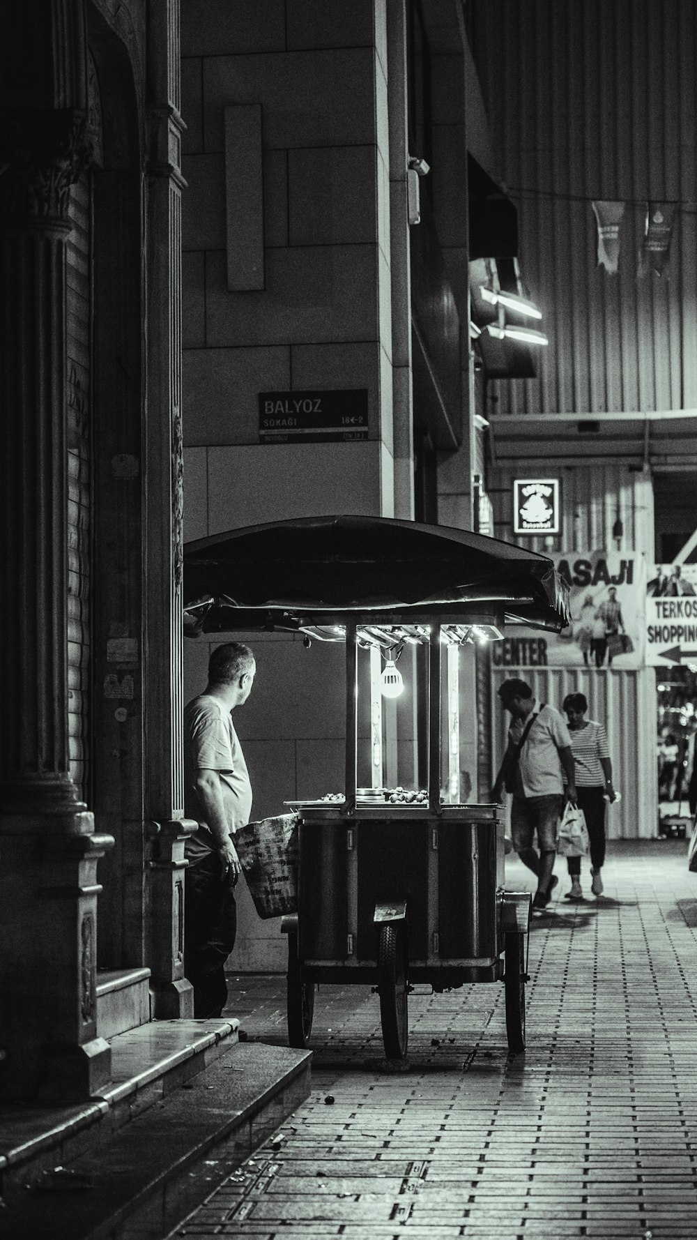 a black and white photo of a boy standing at a bus stop