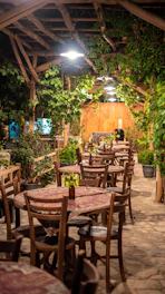 Rustic outdoor grill with sizzling meats and wooden tables under a canopy of trees.