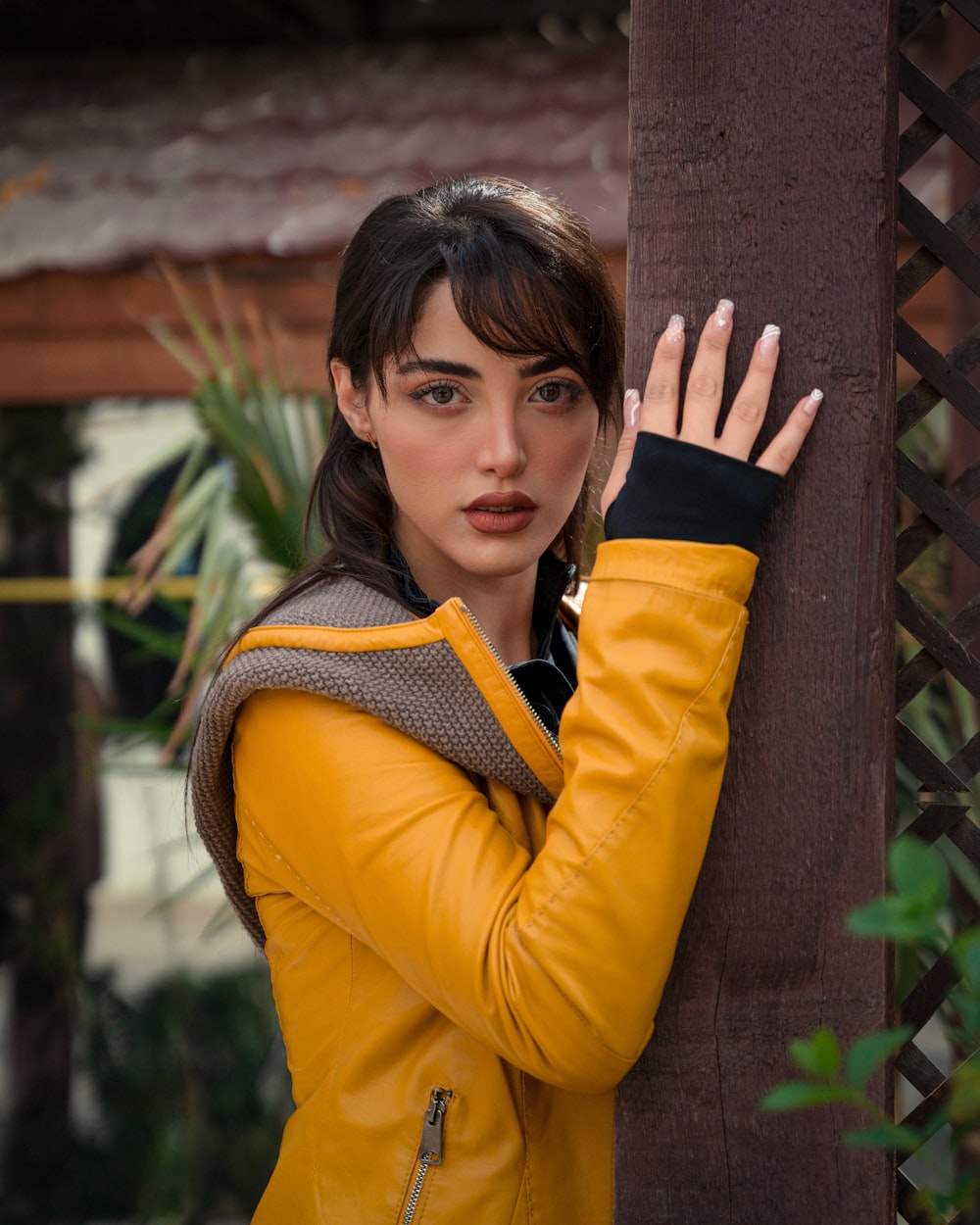 a woman in a yellow jacket leaning against a tree