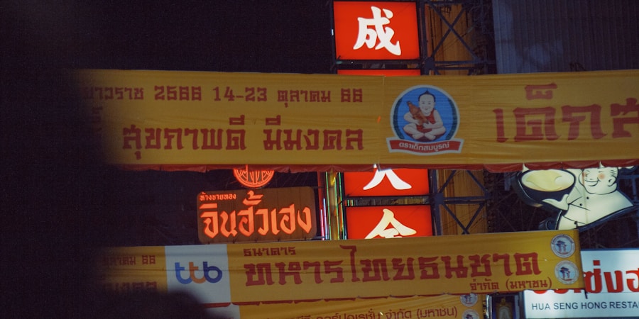A night scene featuring several brightly lit banners and signs with Thai writing. Prominent colors include red and yellow, with white text and illustrations. Logos and advertisements are visible. A cartoon character is depicted holding a bowl, and there is a logo with an image of a baby.
