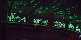 Dark background with green neon signs written presumably in an Asian script, reflecting off a glossy surface.