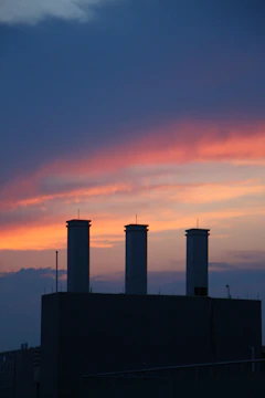 A refinery at sunset with smoke stacks silhouetted against the colorful sky.