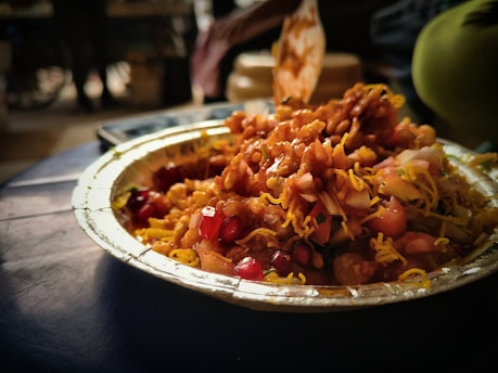 A hand holding a plate of colorful, crunchy chaat against a lively street background.